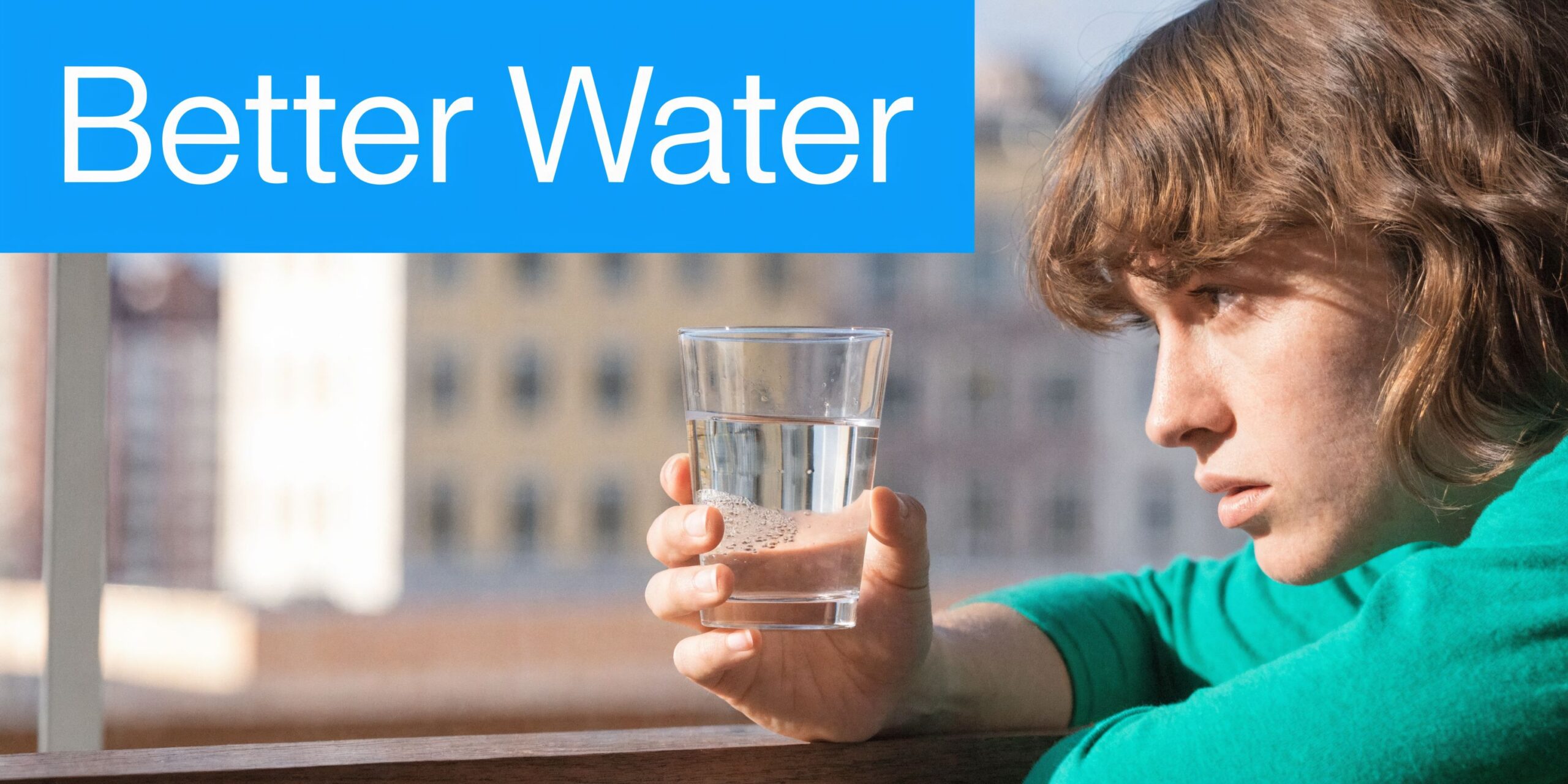 A person looking thoughtful while holding a glass of clear water in front of a blurry background.