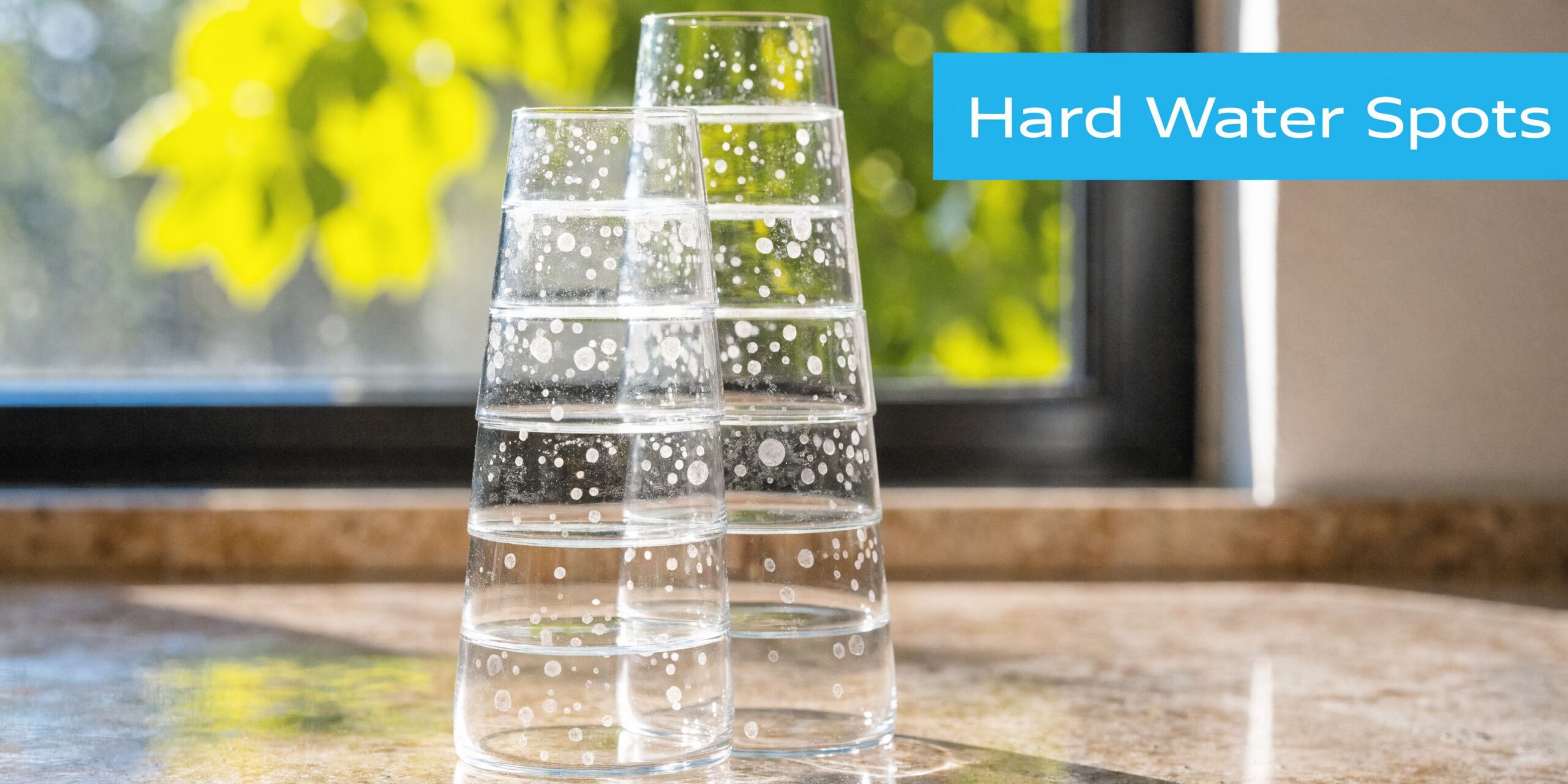 Two stacks of clear drinking glasses covered in white calcium mineral deposits on a marble countertop.