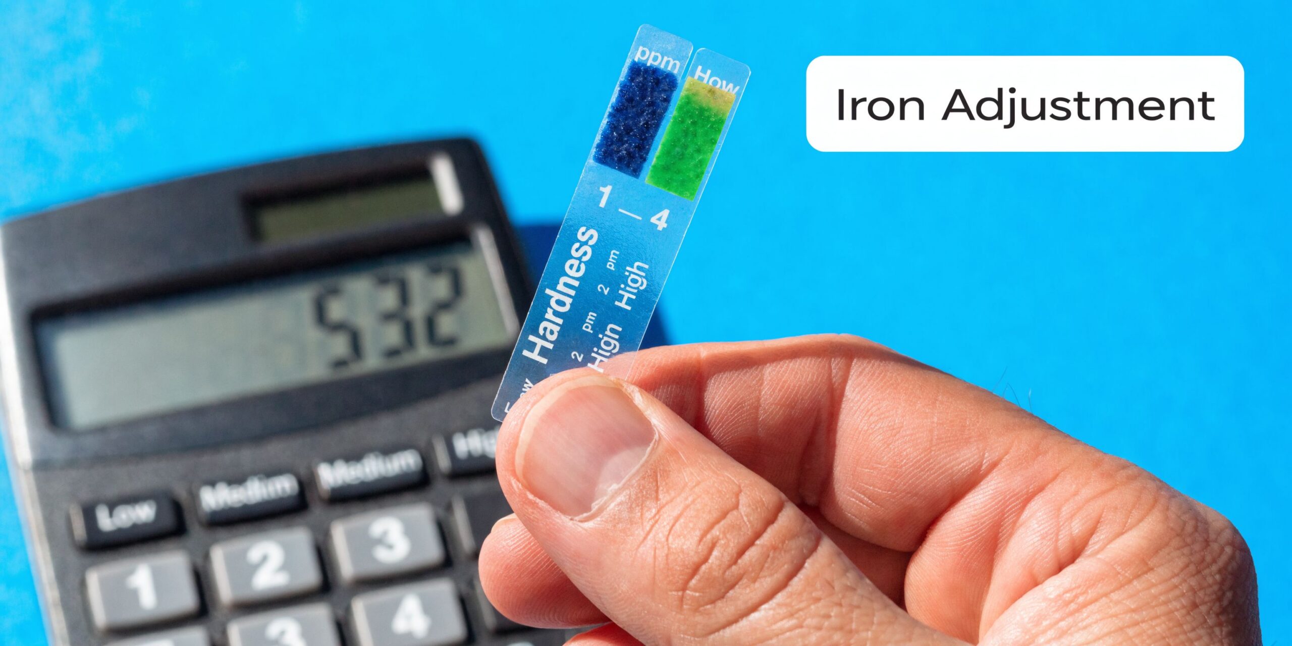 A hand holds a water hardness test strip next to a calculator with the number 532 displayed.